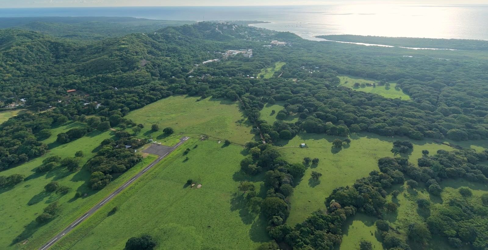 Aerial photograph of the El Llano plain: green pastures, the Tamarindo airstrip and the Pacific coast beyond